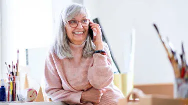 A woman with gray hair smiles as she talks on the phone.