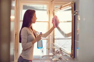 Woman cleaning bathroom mirror